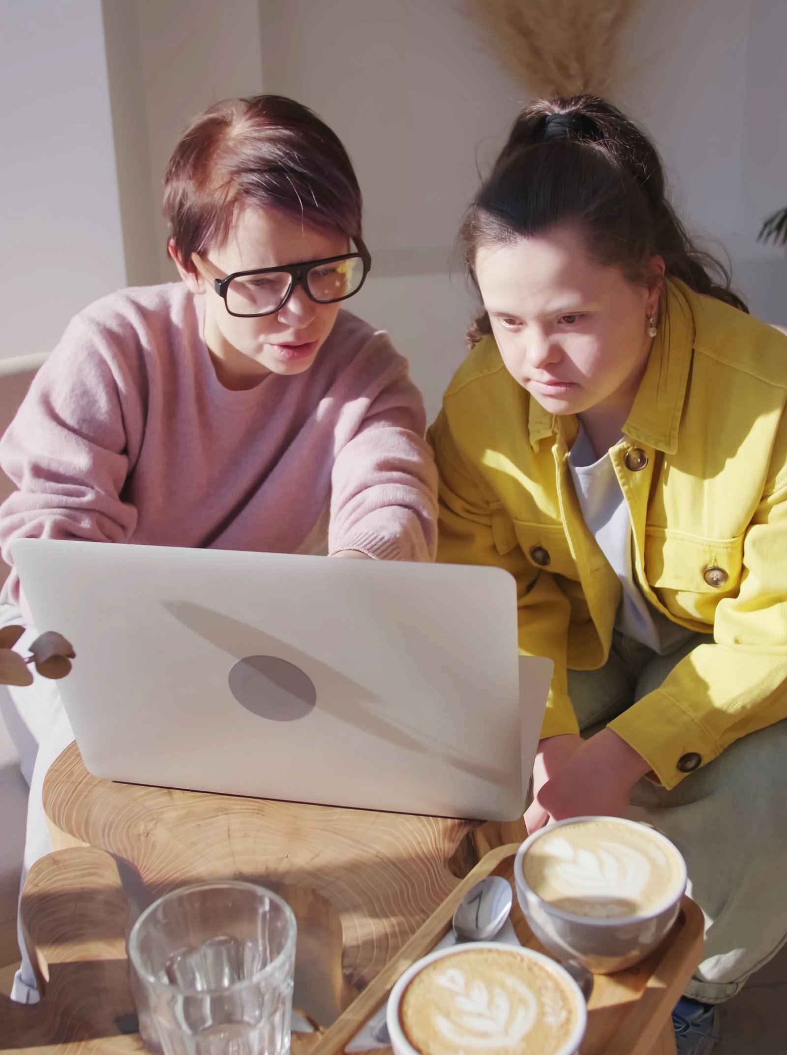 two people sitting together at a laptop at a table in a coffee shop